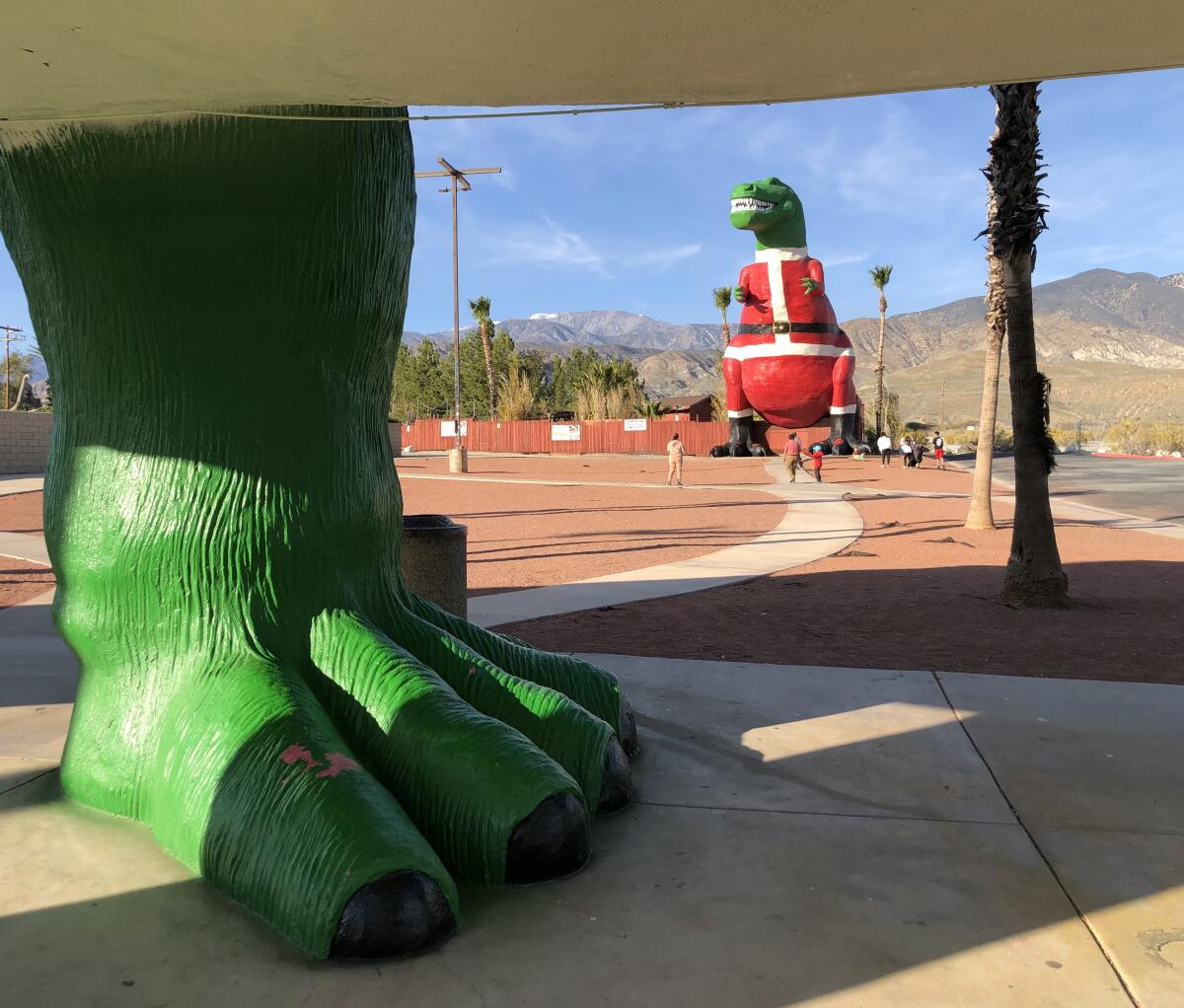 A large dinosaur foot is shown in the foreground with a large T-rex in a Santa suit in the background.