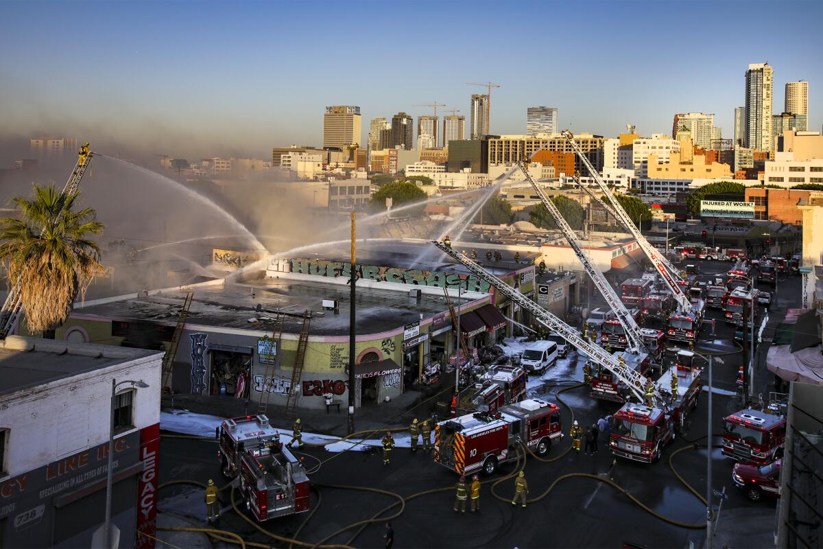 Water is sprayed from multiple fire trucks and ladders are extended over a Fashion District building.