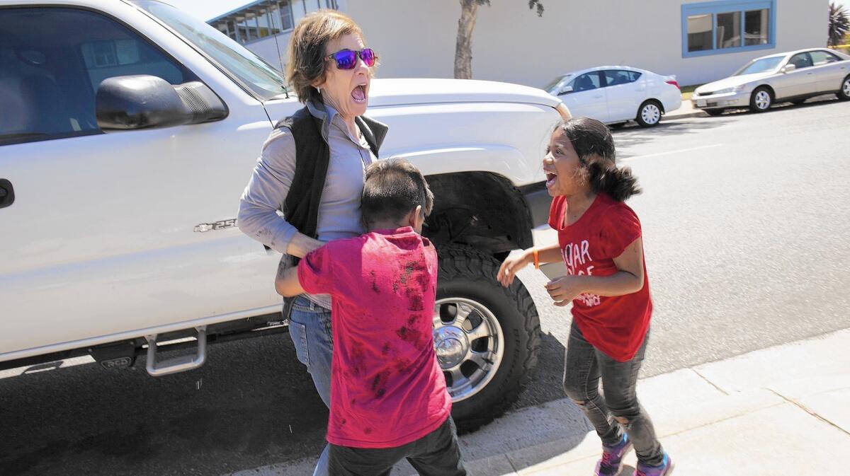 Newport Mesa Unified School District Board Member Karen Yelsey reacts as Whittier Elementary School fourth graders Giovanni Castillo, bottom, and Maria Leon, both covered with mud, give her a hug as they celebrate Earth Day with a mud balling event at Newport Banning Land Trust in Costa Mesa on Tuesday. The event is an effort to build the NBLT nursery and restoration program for Newport Banning Ranch.