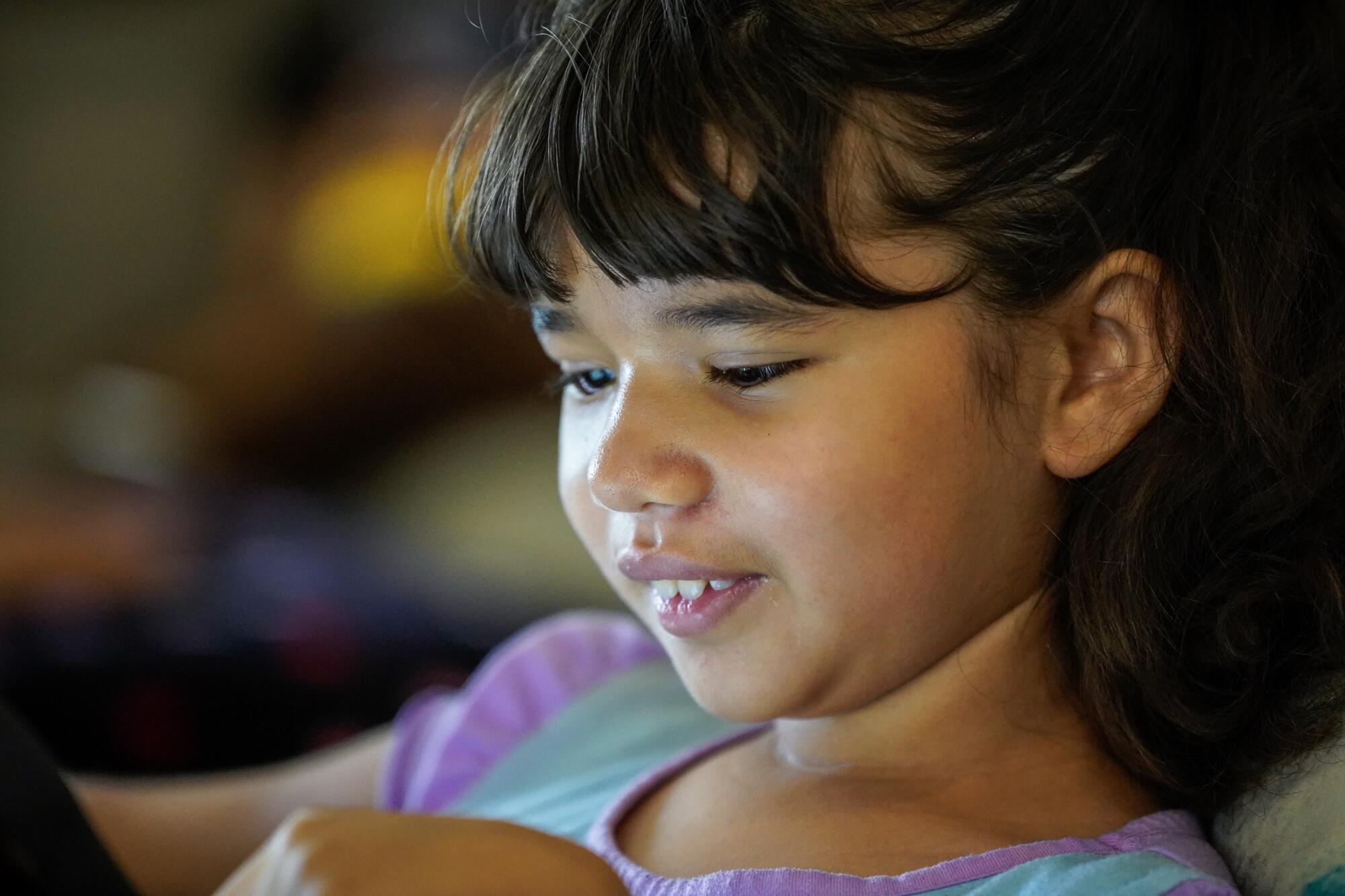 The smiling face of a girl playing on her tablet.