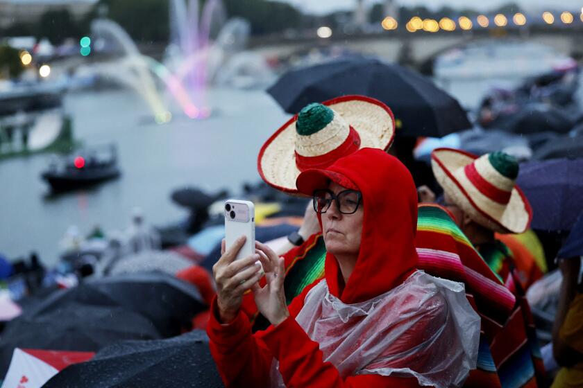 Una espectadora toma una foto con su celular mientras los deportistas pasan en barcos por el río Sena durante la ceremonia de inauguración de los Juegos Olímpicos de 2024 en París, Francia, el viernes 26 de julio de 2024. (Stefan Wermuth/Pool Photo via AP)