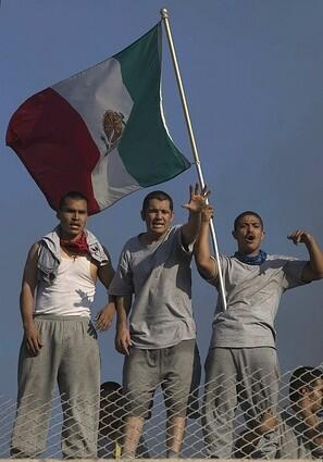 Inmates scream from the roof of a building and wave a Mexican flag.