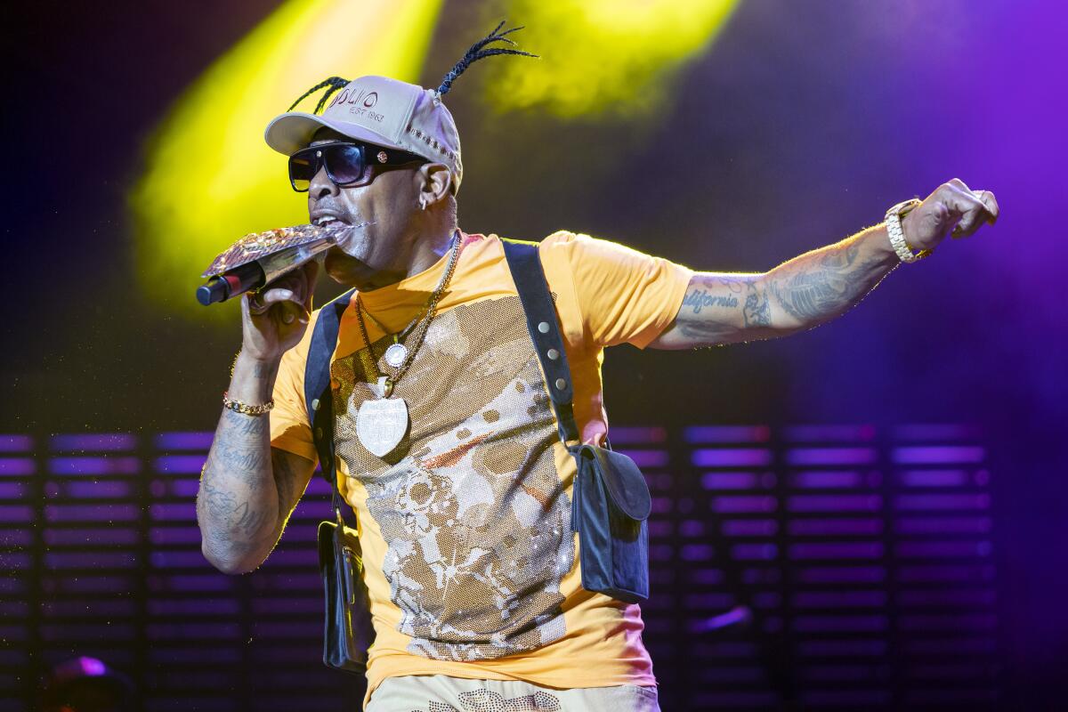 A man with tattooed arms, a print shirt, sunglasses and a hat performs.