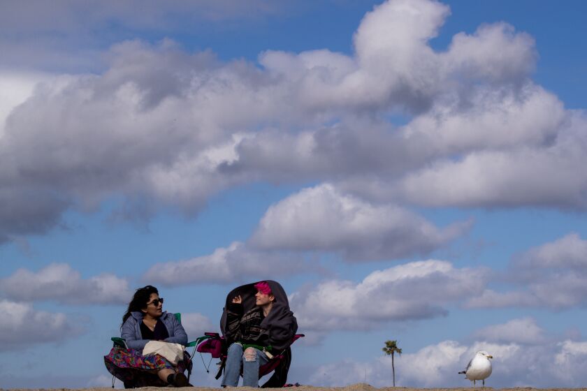 Seal Beach, CA - February 13: Gio Barajas, left, and Andy Lime, both of Avalon, bundle up while sitting on the beach amidst cool windy weather and cloudy skies at Seal Beach Monday, Feb. 13, 2023. (Allen J. Schaben / Los Angeles Times)