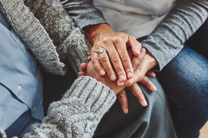 Female healthcare worker holding hands of senior man at care home, focus on hands.