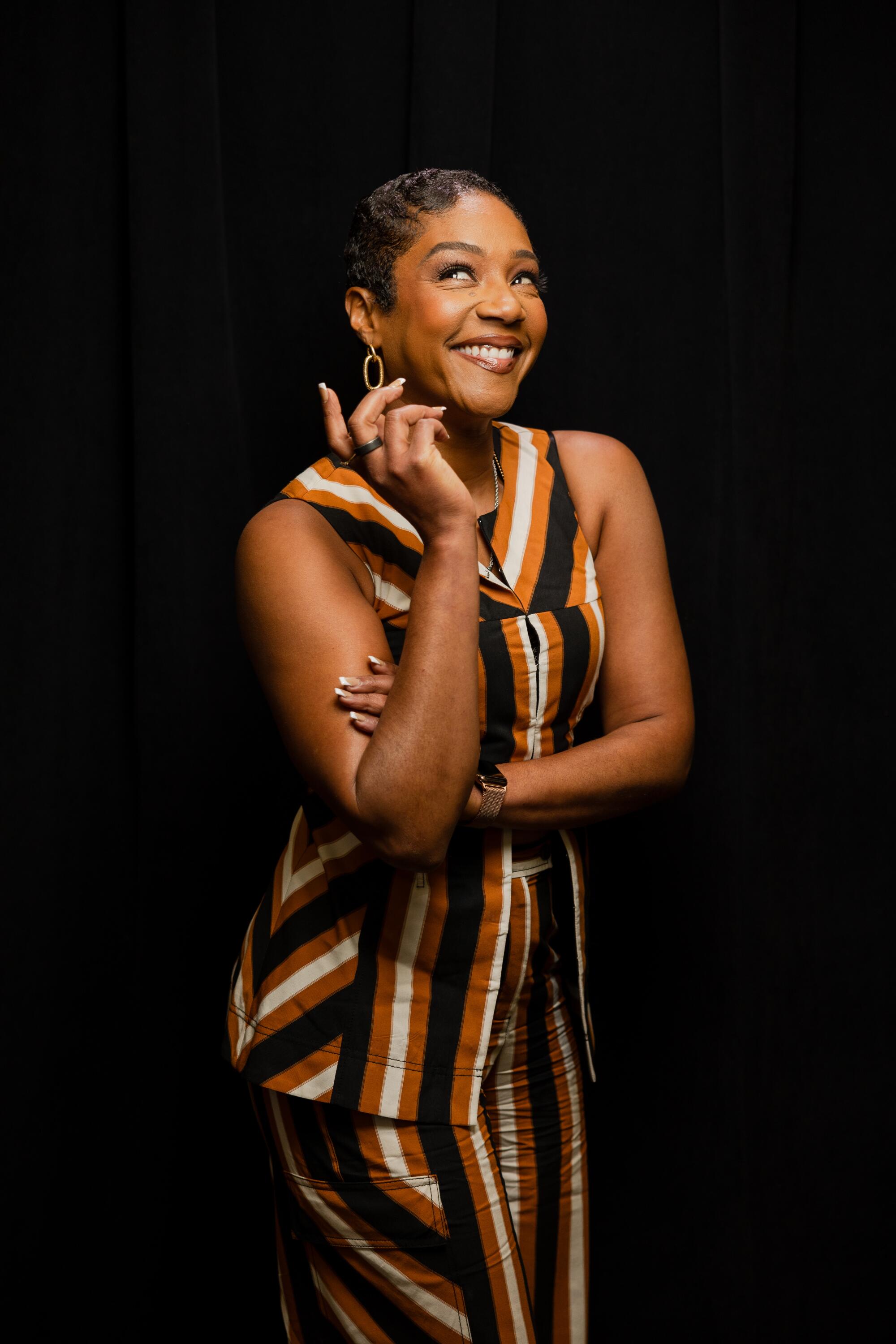 A woman smiles and stands against a black background.
