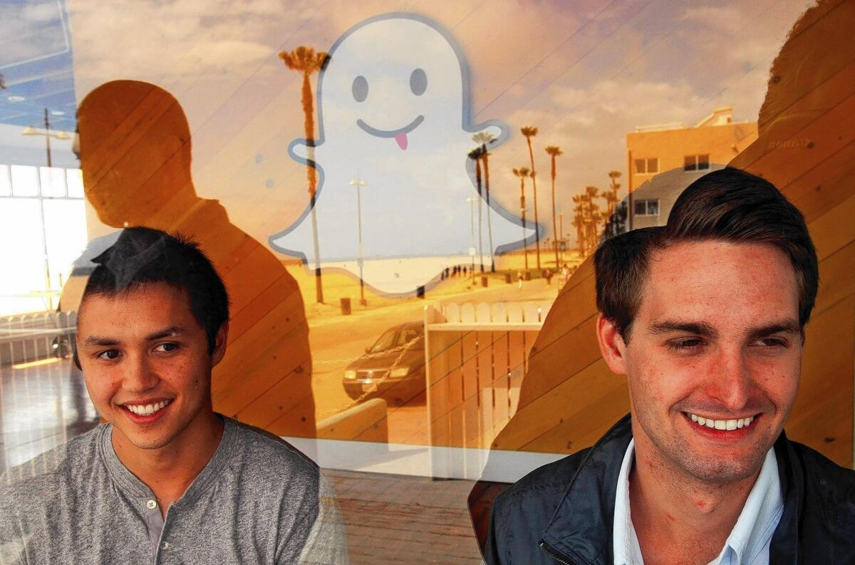 Snapchat founders Robert Murphy, left, and Evan Spiegel are seen through a window of the company's office in Venice. The Snapchat logo, mounted on a wall, seems to float between Murphy and Spiegel.