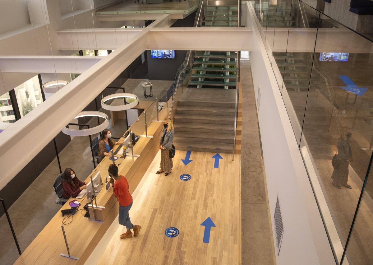 Aerial angle of people talking to a receptionist in an office building with lots of social distancing precautions