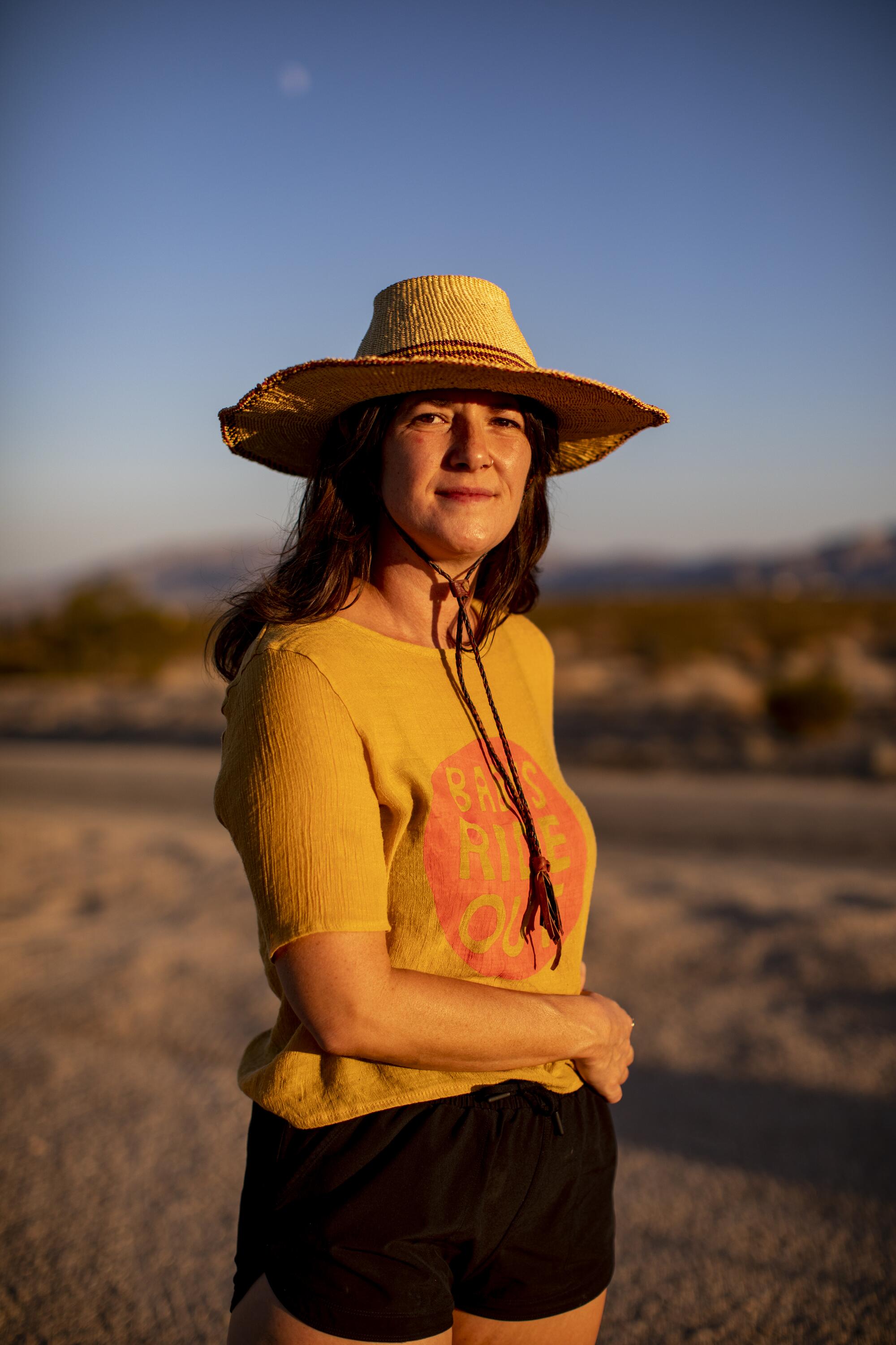 Author Claire Vaye Walkins wears a straw hat, yellow T-shirt and black shorts in the desert.