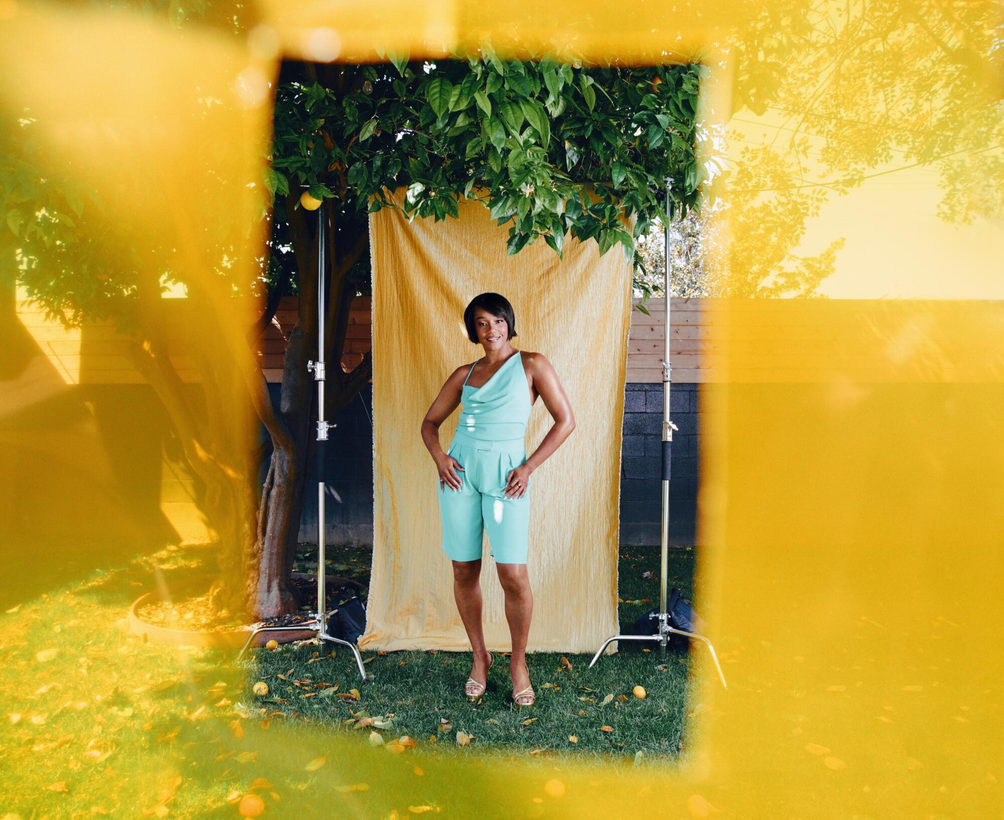 Tiffany Haddish in a mint green romper standing in front of a yellow backdrop under a tree