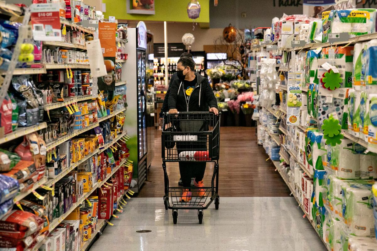 A shopper at an Albertstons grocery store in Los Angeles pushes a cart while glancing at shelved items.