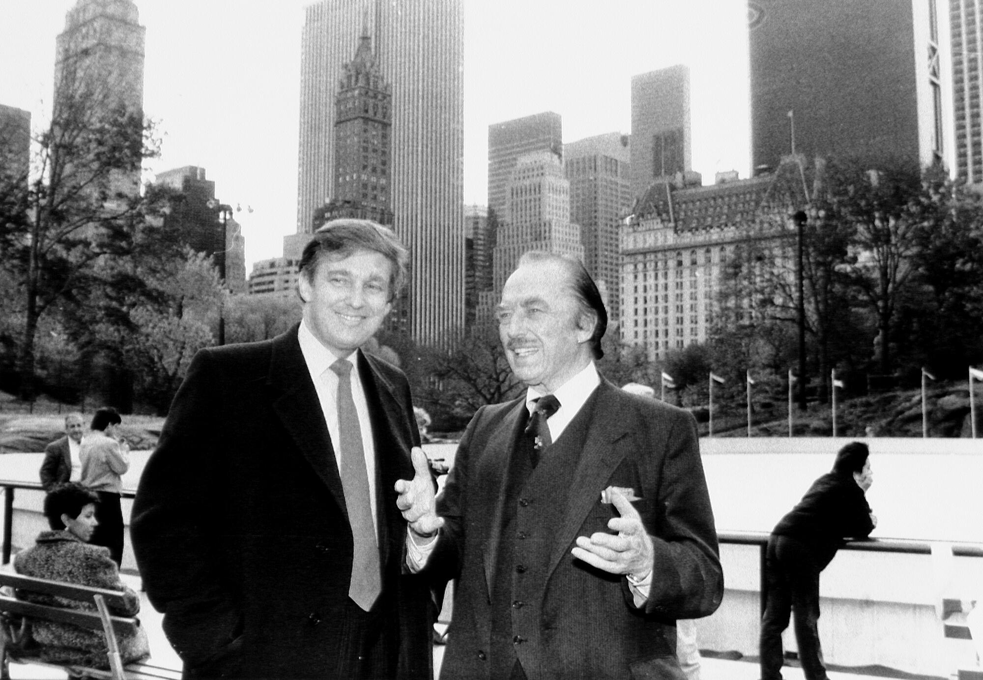 Two men in suit and tie, both smiling, with skyscrapers in the background