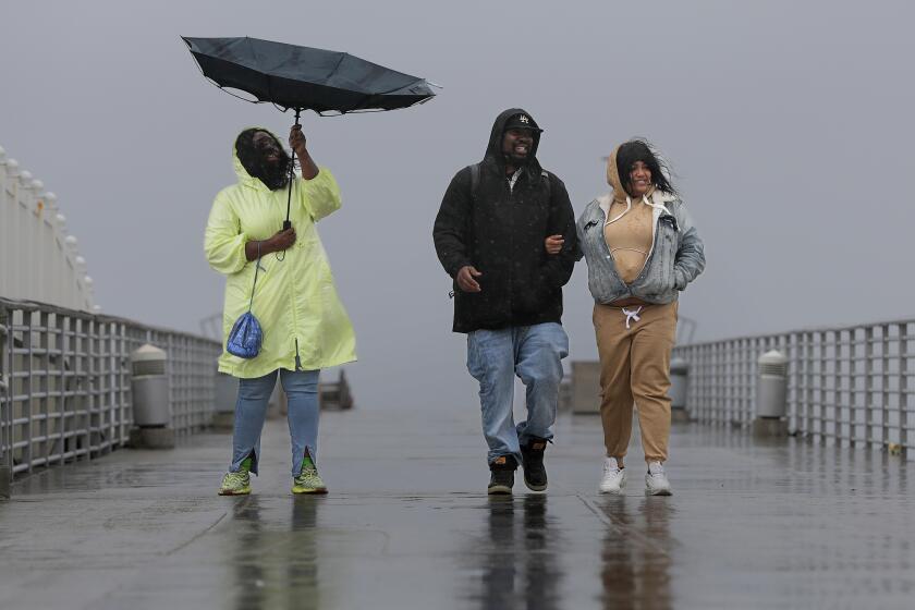 HERMOSA BEACH-CA-MARCH 21, 2023: Gerri Watkins, Cornell Hope, and Meeko Shamel, from left, walk the Hermosa Beach Pier in the rain on March 21, 2023. (Christina House / Los Angeles Times)