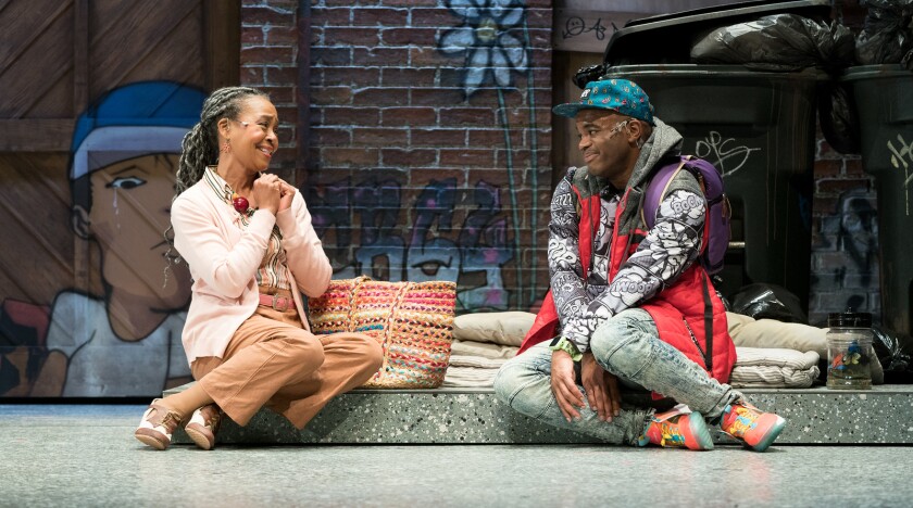 In a scene from a play, two people are sitting on a curb.