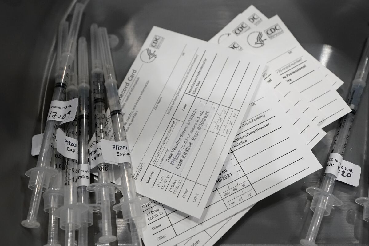 Syringes with doses of the Pfizer COVID-19 vaccine, are shown next to vaccination cards, Saturday, March 13, 2021, on the first day of operations at a mass vaccination site at the Lumen Field Events Center in Seattle, which adjoins the field where the NFL football Seattle Seahawks and the MLS soccer Seattle Sounders play their games. The site, which is the largest civilian-run vaccination site in the country, will operate only a few days a week until city and county officials can get more doses of the vaccine. (AP Photo/Ted S. Warren)