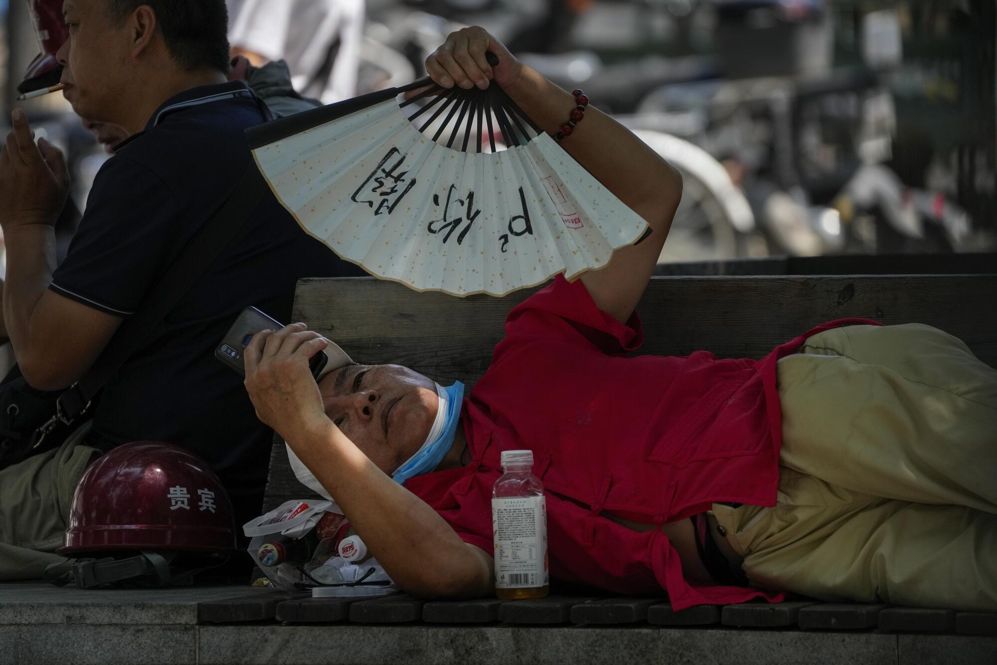 A man cools himself with a fan while browsing his phone 