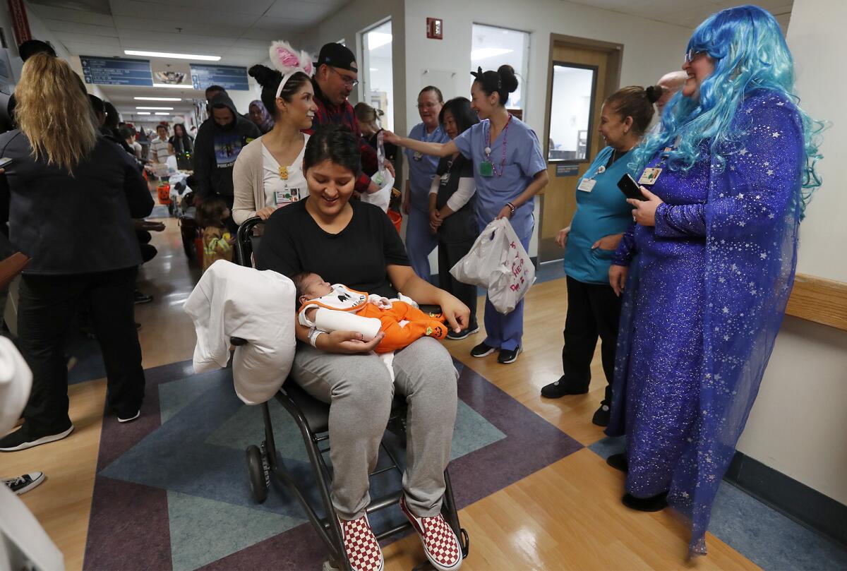 Andrea Amaro takes her 2-week-old son Damian, dressed in a pumpkin costume, to receive treats from doctors and staff members during a trick-or-treat parade Thursday morning at Fountain Valley Regional Hospital & Medical Center.