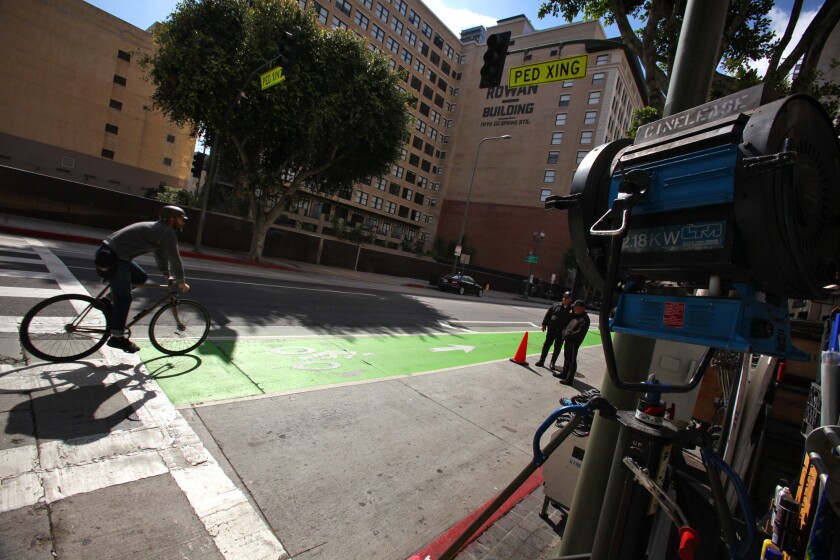 Production equipment is set up for a television shoot as cyclists pass by in the bright green bike lane in the 400 block of Spring Street in March. The city is now in the process of repainting the strip a darker green to appease Hollywood reps who said the brighter color interfered with filming.