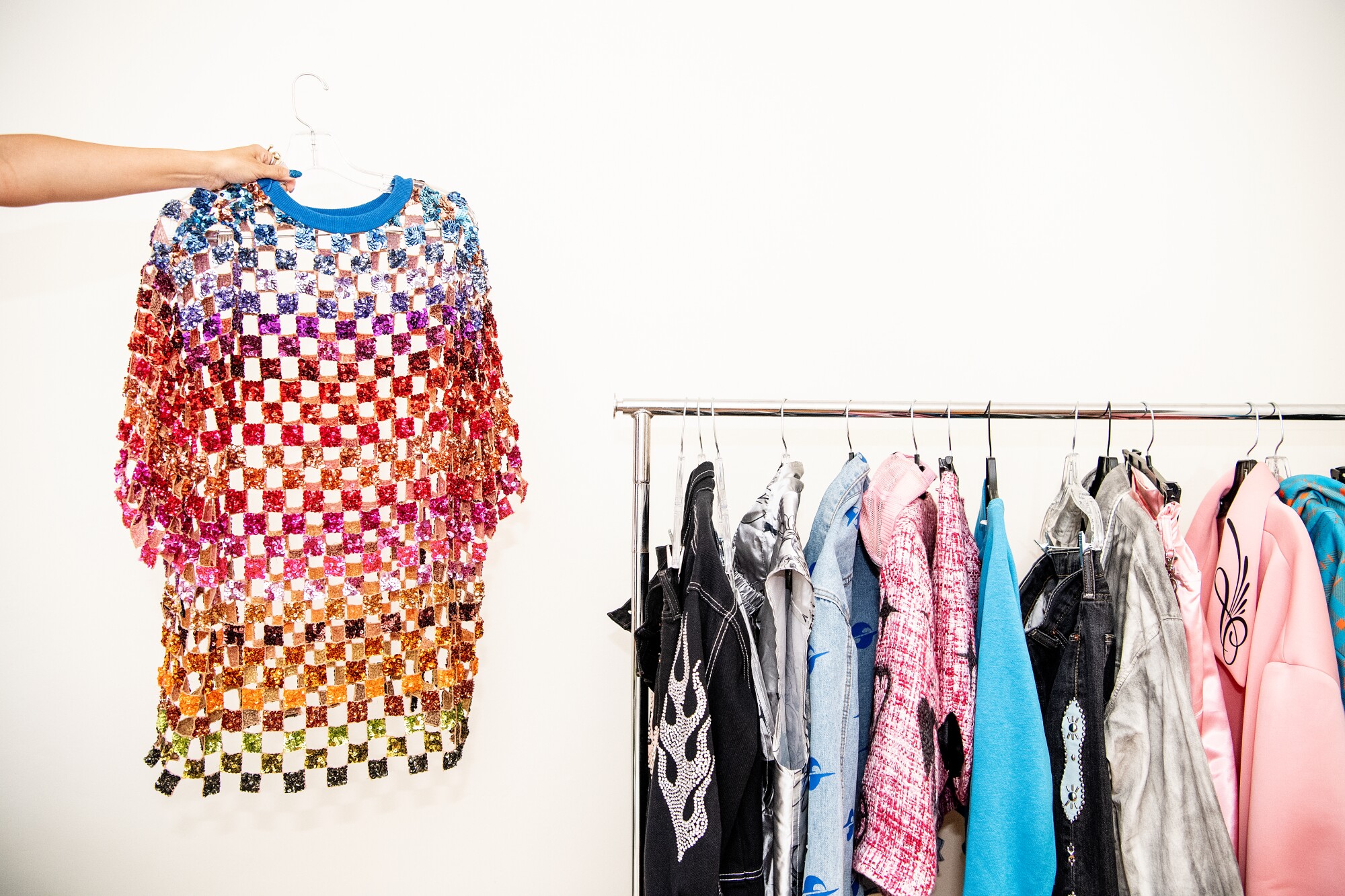 Stylist Keyla Marquez holds a colorful sequined shirt next to a clothes rack