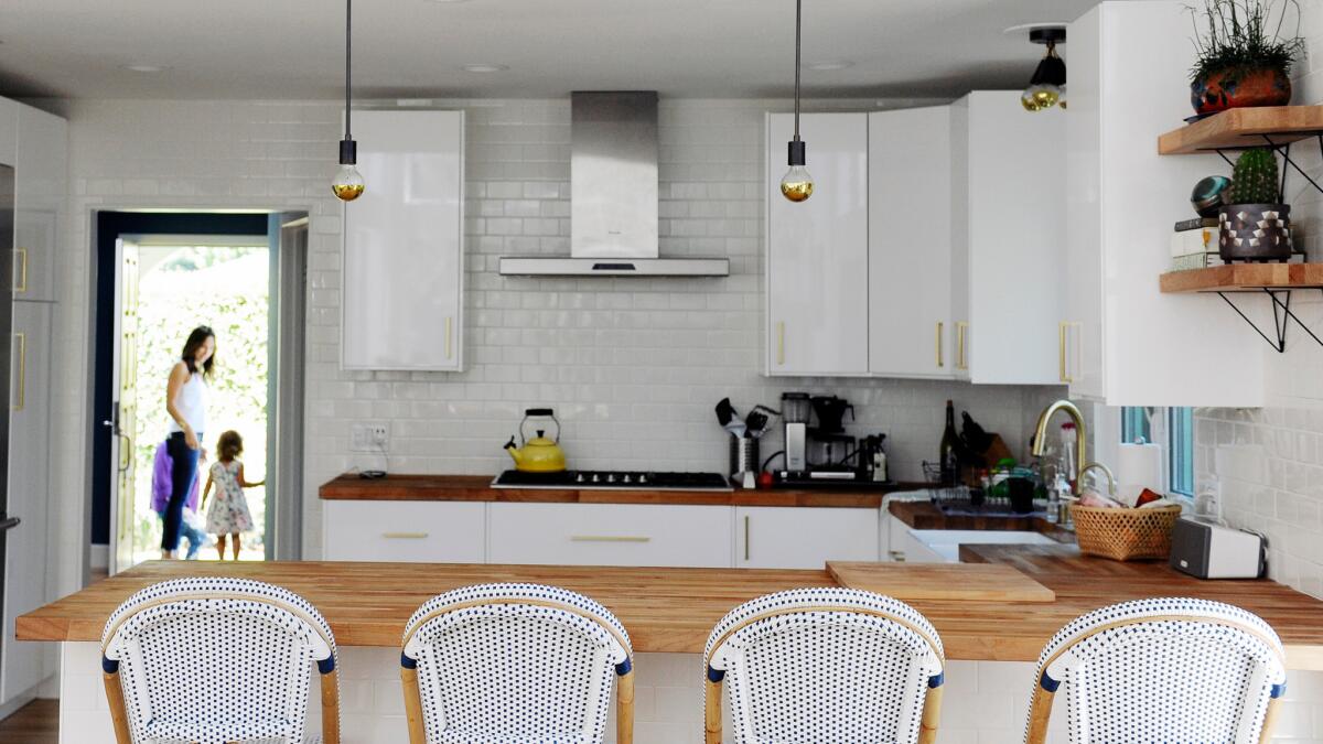 The sunny white kitchen features high gloss cabinets from Ikea and bistro barstools from Serena and Lily.