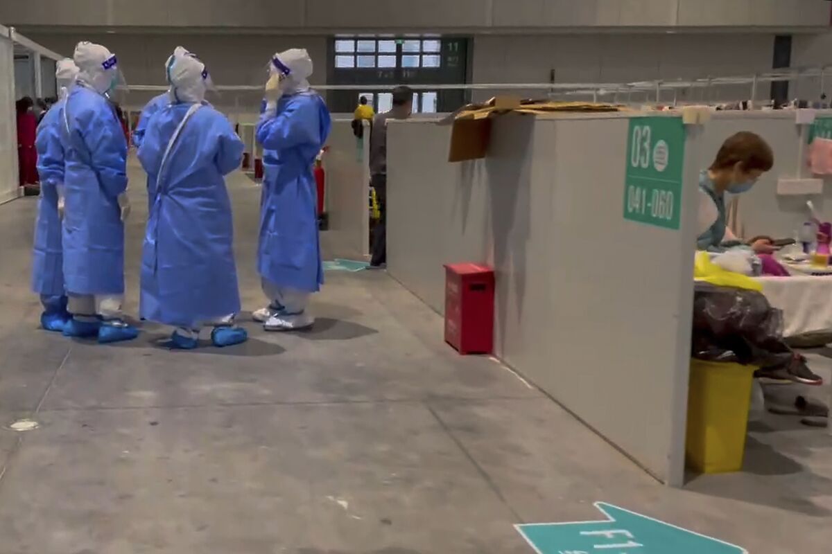 In this image taken from video provided by Beibei, who asked to be identified only by her given name, medical workers wearing protective suits chat as a resident takes a rest at the National Exhibition and Convention Center on April 15, 2022, in Shanghai. The convention center converted to a quarantine facility set up for people who tested positive but have few or no symptoms. (Beibei via AP)