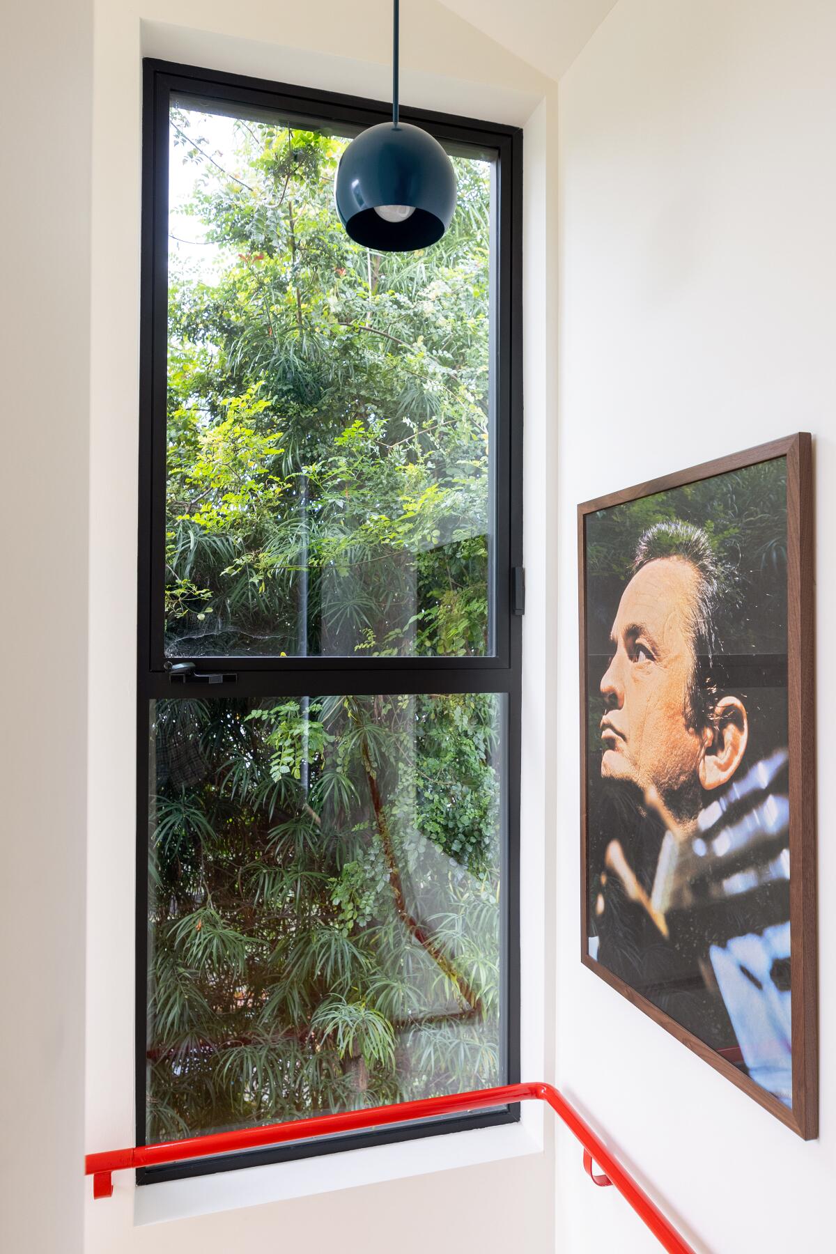 A tree can be seen from a window. On the wall hangs a painting of a man's face. 