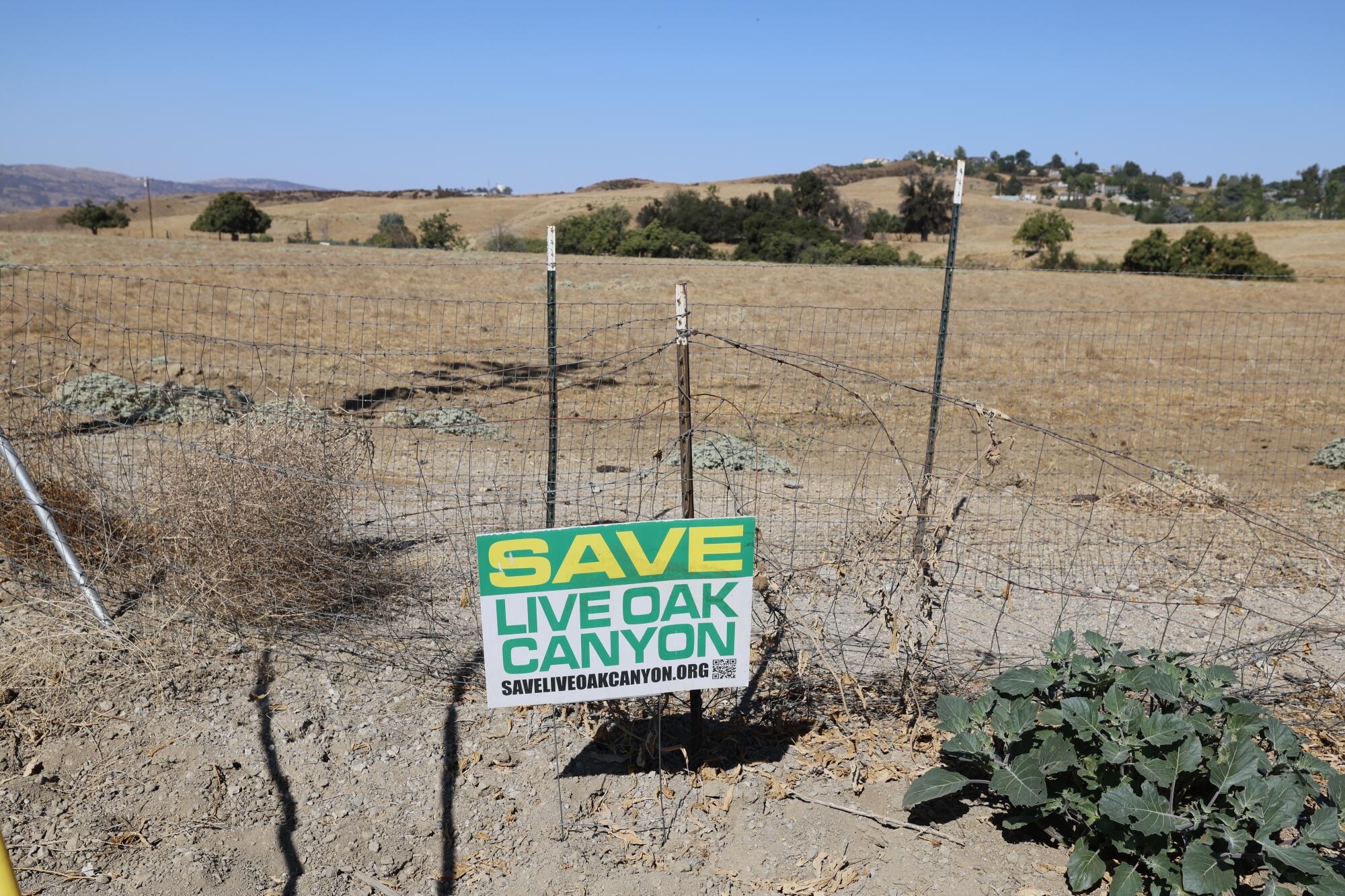 A sign posted to a wire fence reads "Save Live Oak Canyon."