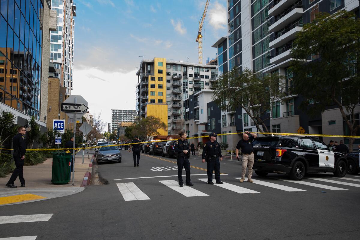 Police stand outside yellow crime-scene tape on a street lined with condos