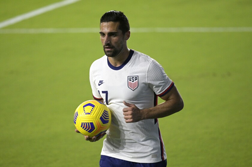 Sebastian Lletget, in USA jersey, holds the soccer ball on the field.