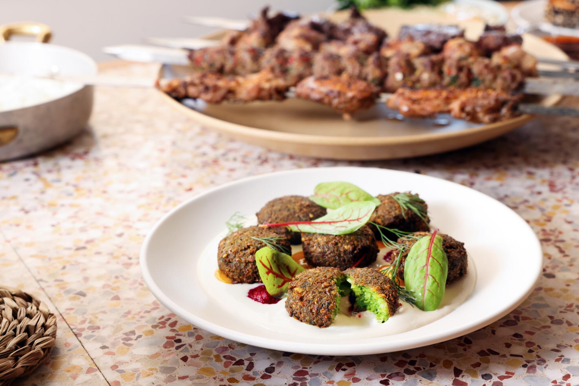 The green falafel dish with pieces of falafel broken open to show the green inside.