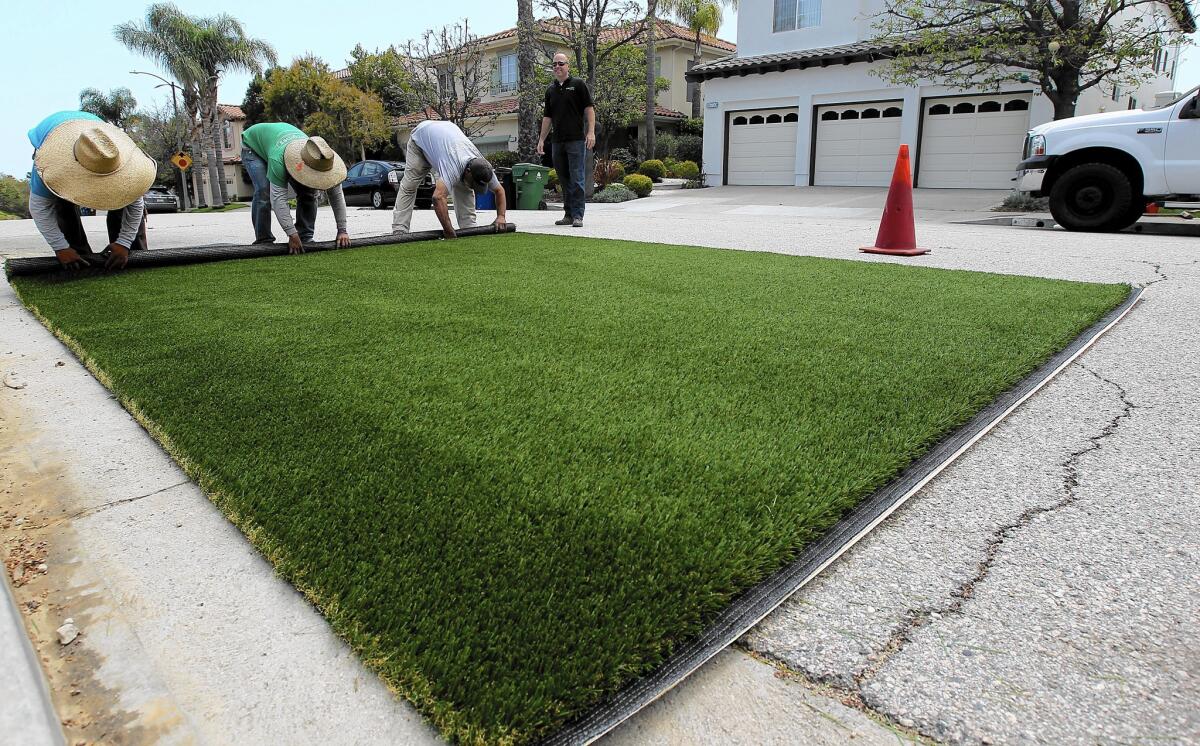 Workers roll up a piece of artificial grass to be installed in the backyard of a Pacific Palisades home in May.