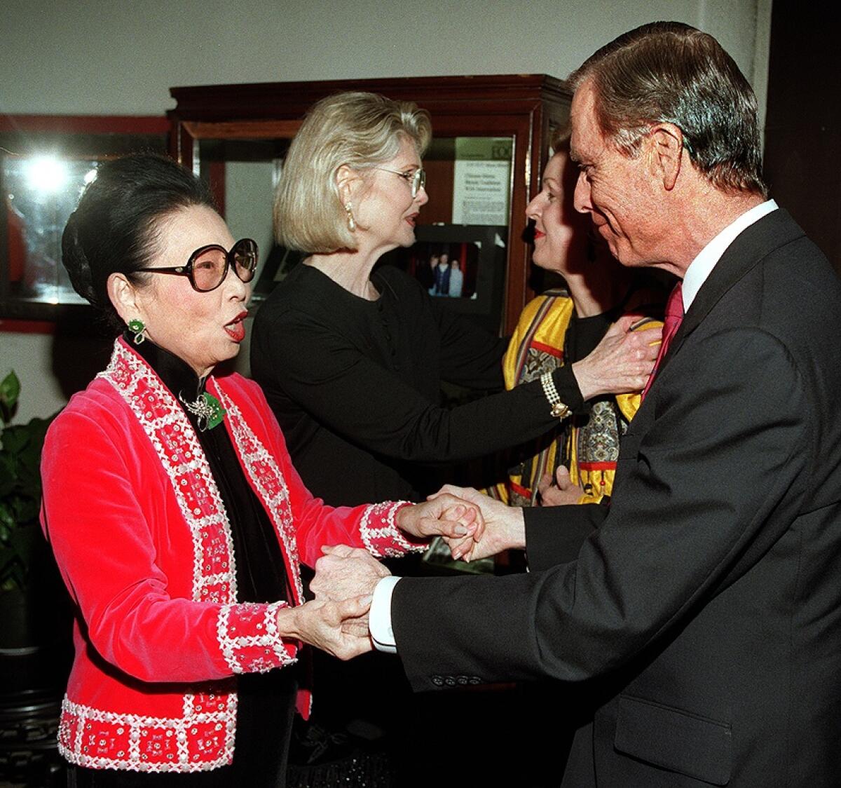 Madame Wu and then-Gov. Pete Wilson hold hands as they face each other.