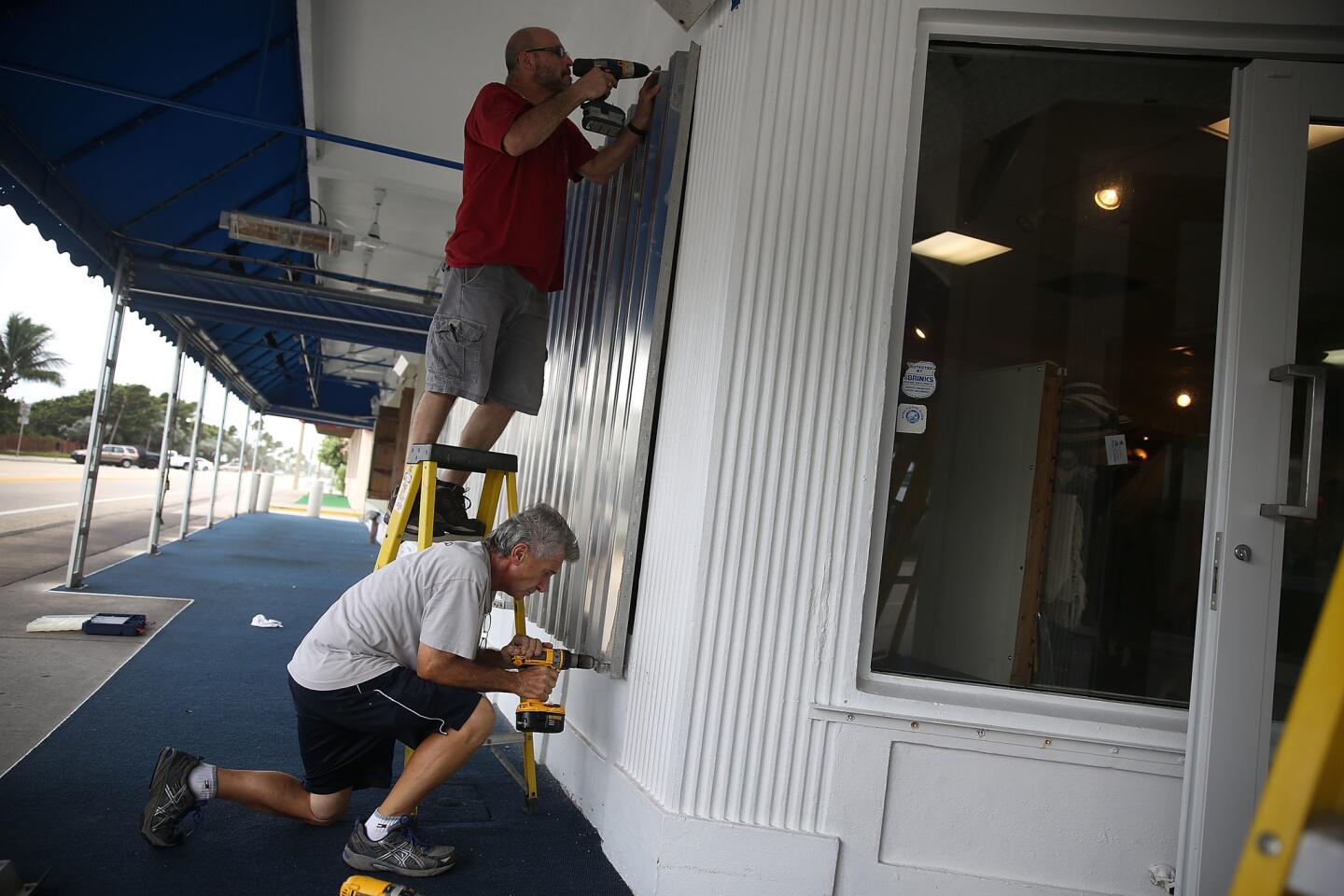 Pat Lena and Frank Capano (bottom) put up hurricane shutters as they prepare a shop for Hurricane Matthew on October 6, 2016 in Delray Beach.