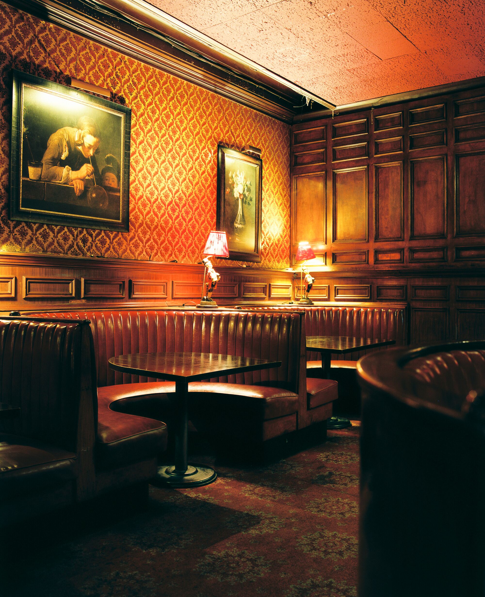 A photo of brown-red booths in a red-lit restaurant with a reproduction of a Chardin painting on the wall.