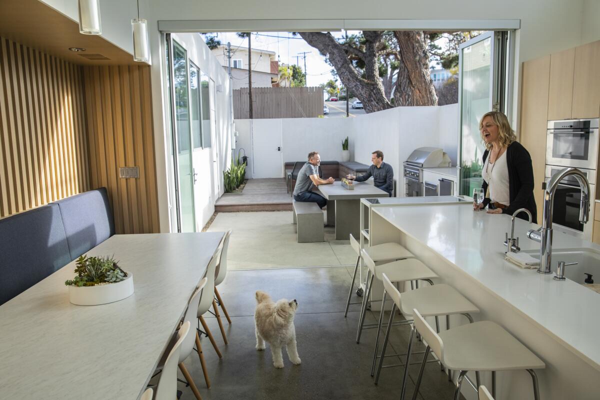 After the remodel: Charlie pauses to see what homeowner Alison Goad is up to, while in the kitchen, where the island and dining table enhance the linear flow out to the back patio, which is shaded by a large Italian stone pine tree.