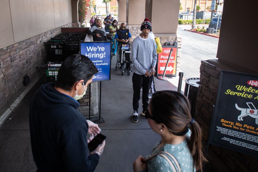 LOS ANGELES, CALIF. - MARCH 22, 2020: Grocery store worker Enrique (left) stands at the door of Ralphs grocery store in Westchester letting in only a few shoppers at a time on Sunday, March 22, 2020 in Los Angeles, Calif.. This Ralphs location is implementing social distancing guidelines for its customers. The store is placing social distancing markers every six feet and limiting the number of customers it allows in to shop to help with social distancing due to the Coronavirus pandemic. (Jason Armond / Los Angeles Times)