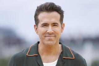 Ryan Reynold grinning wearing a green collard shirt. 