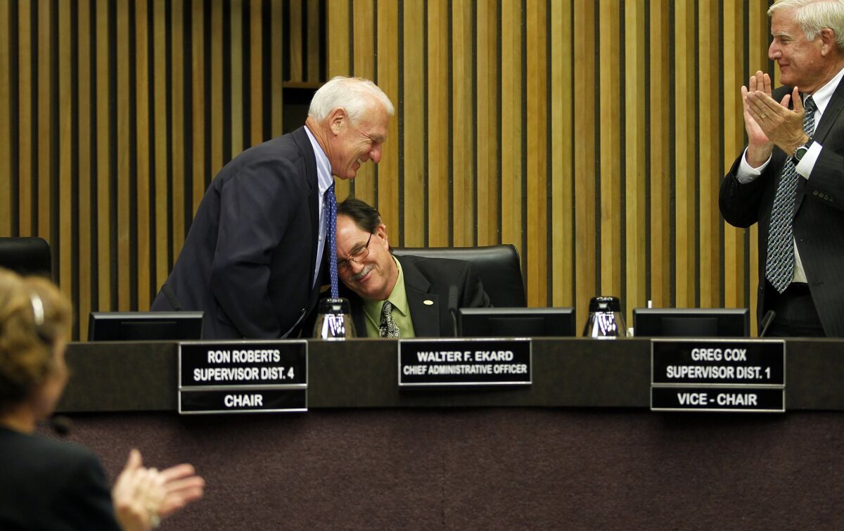 Supervisor Ron Roberts (left) gives a hug to Walter Ekard, county CAO, as Ekard announces his retirement during a meeting of the County Board of Supervisors on Wednesday in San Diego, California. — Eduardo Contreras