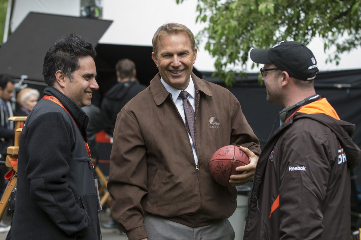 the man holds a soccer ball while two other men talk to him