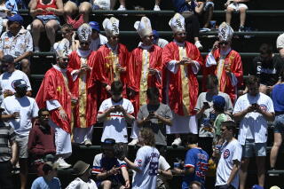 Six fans wearing red and gold robes and white mitres with White Sox logos in the stands among other baseball fans