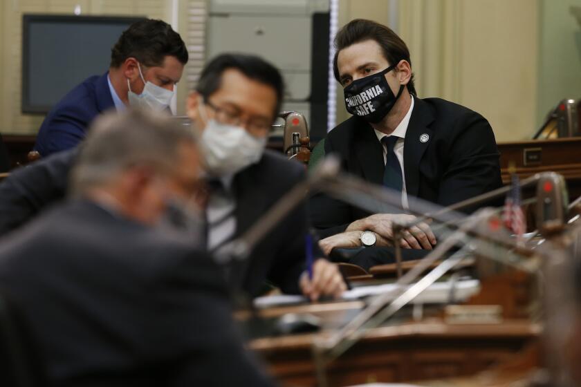 Wearing a face mask reading "California safe," Assemblyman Kevin Kiley, right, R-Granite Bay, attends a hearing of the Assembly Transportation Committee in Sacramento, Calif., Monday, May 4, 2020. Assembly members returned to the Capitol on Monday after a nearly six-week layoff due to the coronavirus pandemic. Committee members wore masks, and practiced social distancing by meeting in the Assembly chamber, instead of a smaller hearing room. (AP Photo/Rich Pedroncelli)