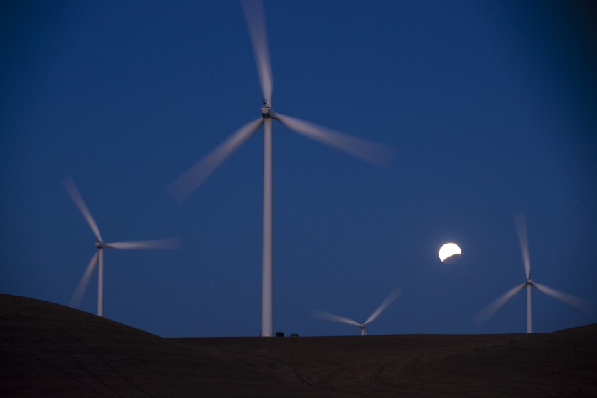 Turbines spin as the blood moon lunar eclipse sets behind the towers of the Shiloh II wind farm on May 26, 2021.