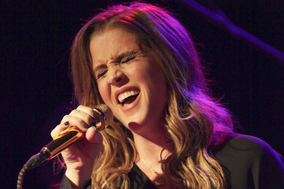 A woman sings with her eyes closed while holding a microphone