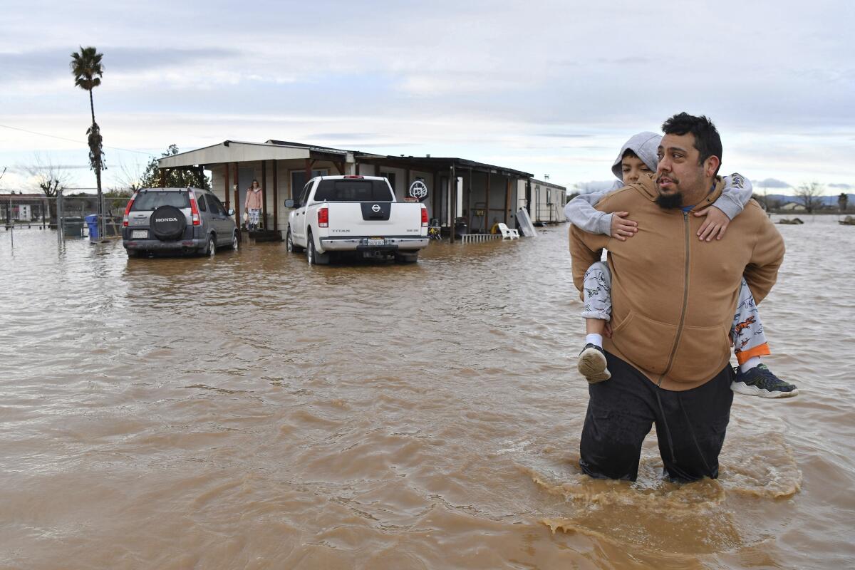 FILE - Ryan Orosco, of Brentwood, carries his son Johnny, 7, on his back while his wife Amanda Orosco waits at the front porch to be rescued from their flooded home on Bixler Road in Brentwood, Calif., Jan. 16, 2023. The National Oceanic and Atmospheric Administration announced Monday, Sept. 11, that there have been 23 weather extreme events in America that cost at least $1 billion this year through August, eclipsing the year-long record total of 22 set in 2020. (Jose Carlos Fajardo/Bay Area News Group via AP)