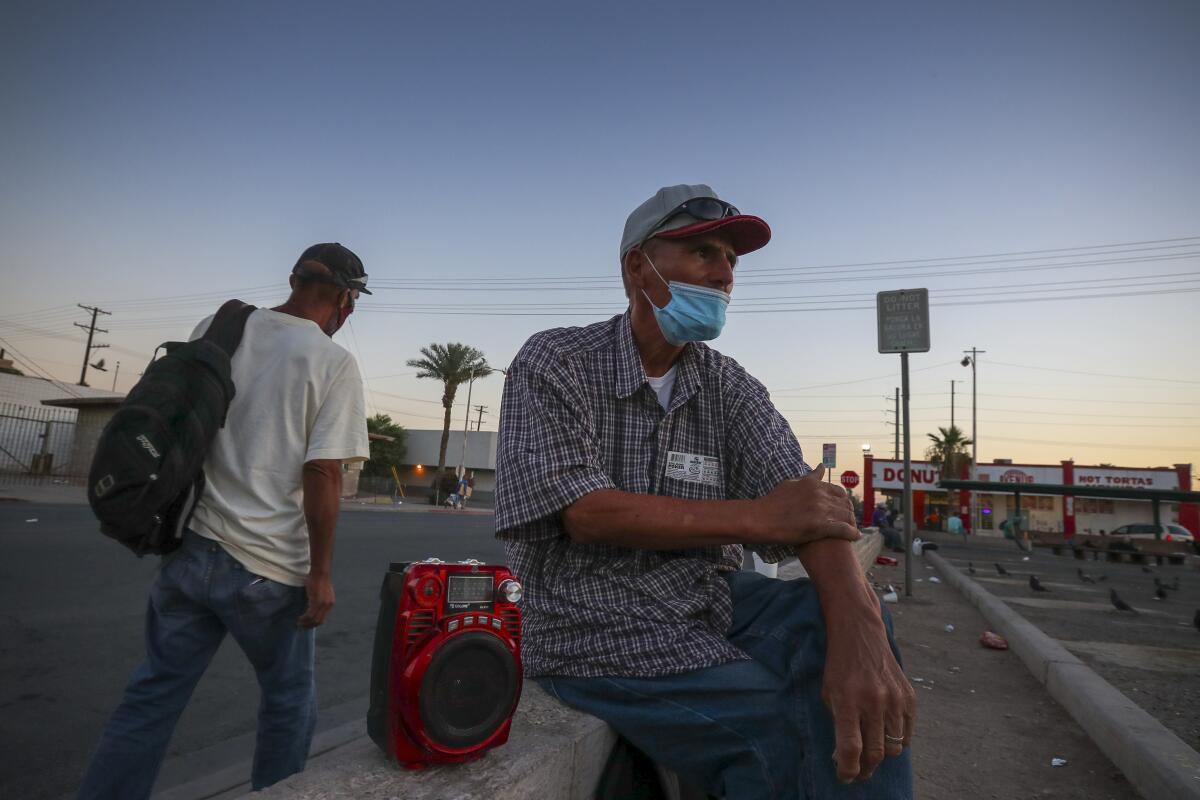 A 65-year-old man in a mask sits and waits for a day labor job in Calexico.