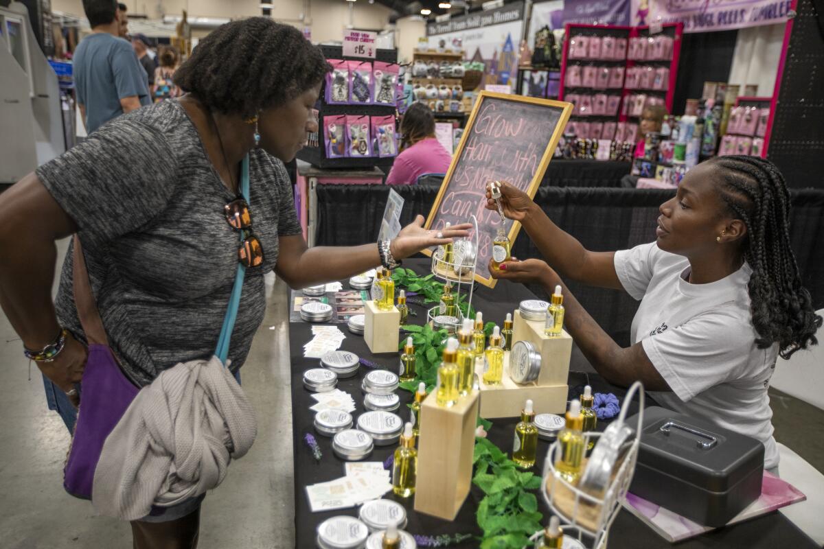 A woman sitting behind a table with products on display dabs liquid from a bottle on a customer's hand.