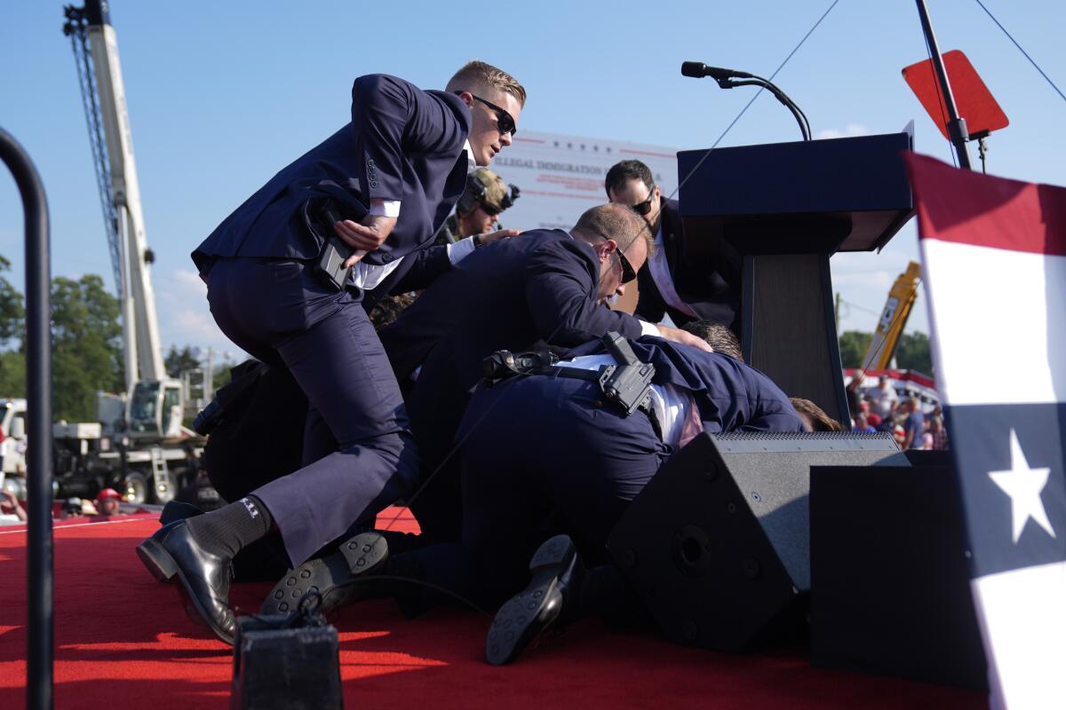 Secret Service agents cover former President Trump near the riser on a red stage