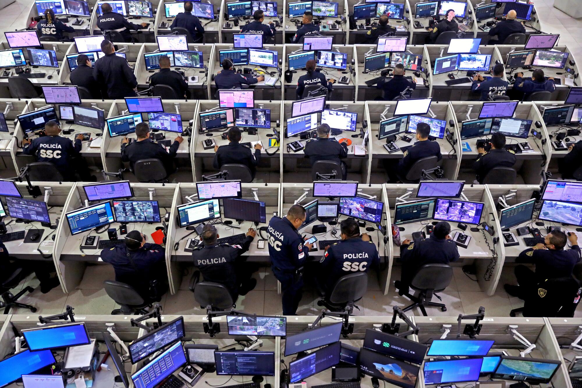 Mexico City police officers sit in rows of cubicles monitoring computer screens.