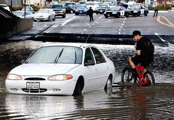 Yeisen Molina ventures out on his bike to check on one of the cars trapped in a pool of rainwater on El Toro Road under the 5 Freeway overpass in Lake Forest.