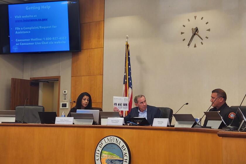 Laguna Beach City Councilman Bob Whalen, center, holds up a handout on wildfire safety measures at a town hall meeting about fire insurance.